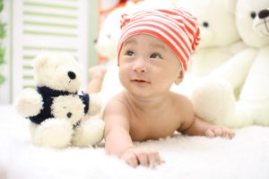 A young baby boy wearing a knit cap is pictured with stuffed animals.